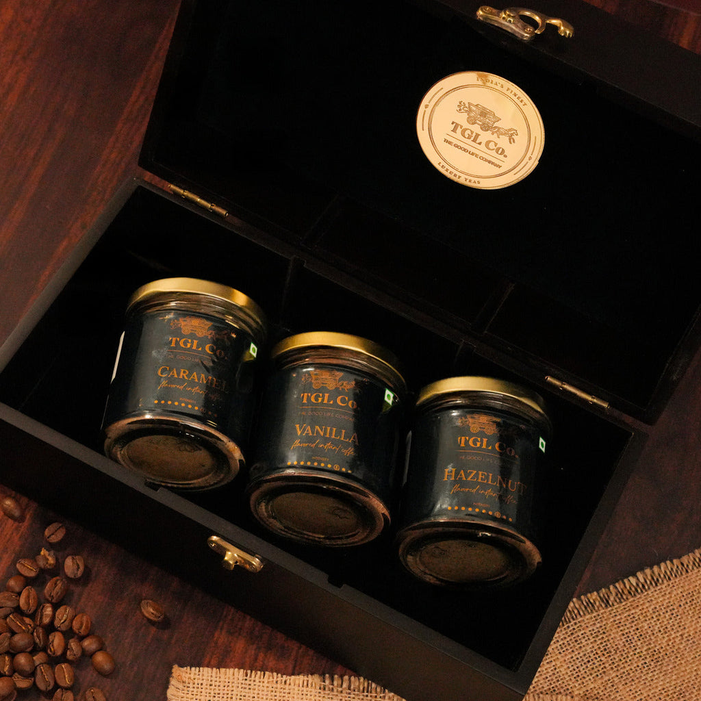 Three jars of TGL Co. coffee in a wooden gift box with coffee beans on a wooden surface.
